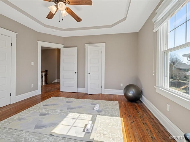 workout room featuring a tray ceiling, plenty of natural light, wood finished floors, and baseboards