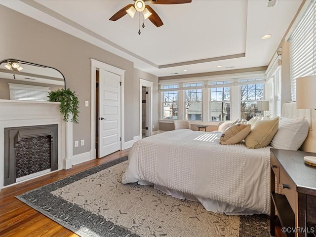 bedroom featuring recessed lighting, a fireplace, wood finished floors, baseboards, and a raised ceiling