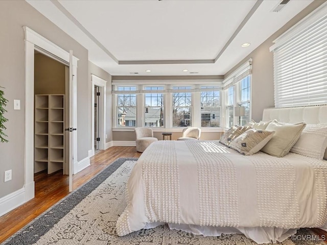 bedroom with a tray ceiling, baseboards, and wood finished floors