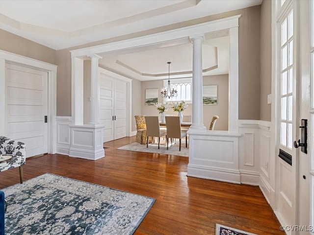 dining room featuring dark wood-type flooring, a raised ceiling, wainscoting, and ornate columns