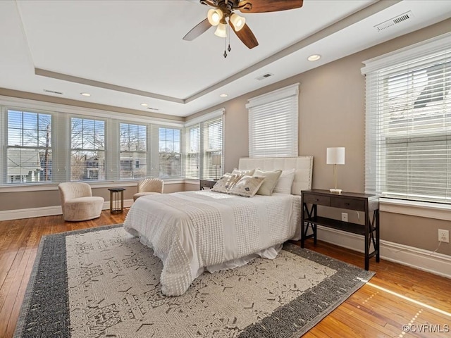 bedroom featuring baseboards, visible vents, a raised ceiling, and hardwood / wood-style floors