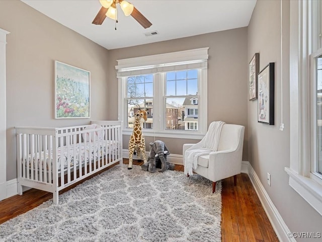 bedroom with baseboards, visible vents, a ceiling fan, wood finished floors, and a nursery area