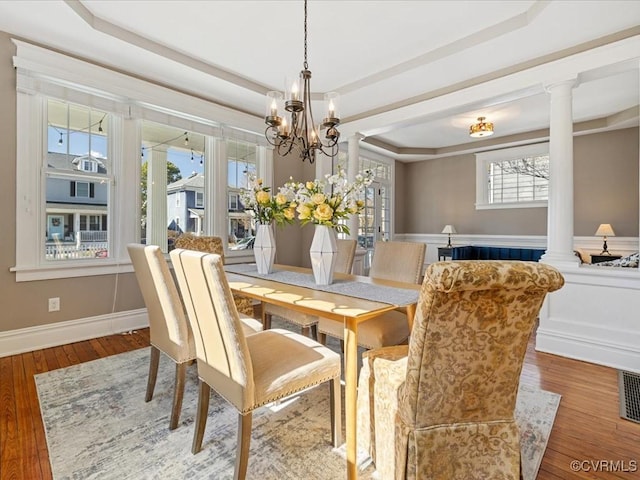 dining room with a wainscoted wall, a tray ceiling, wood finished floors, and ornate columns