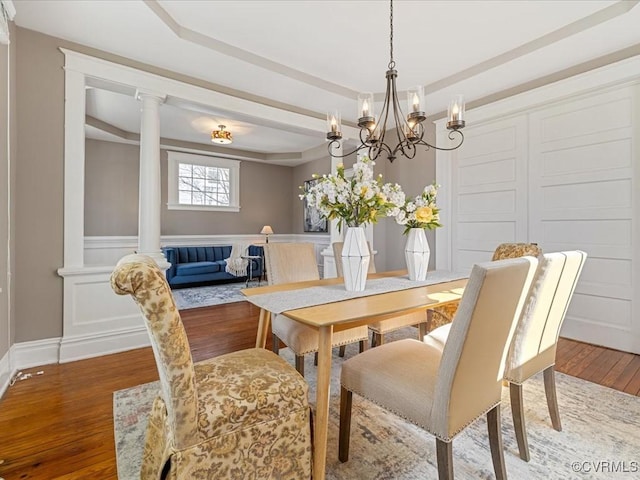 dining space with a raised ceiling, a decorative wall, decorative columns, and wood finished floors