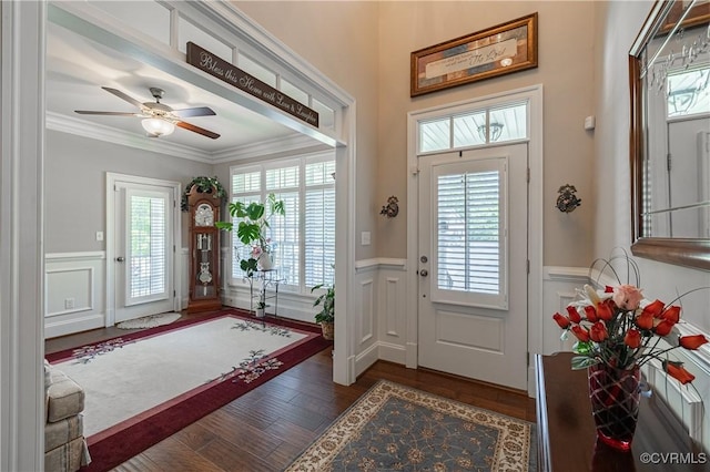 foyer entrance with a decorative wall, wood finished floors, a ceiling fan, ornamental molding, and wainscoting