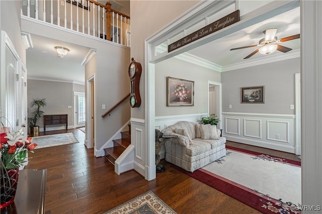 interior space featuring dark wood finished floors, a wainscoted wall, ceiling fan, stairway, and crown molding