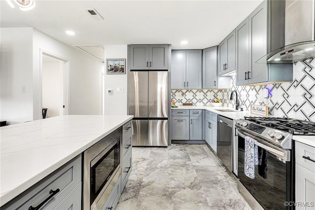 kitchen with visible vents, gray cabinets, a sink, appliances with stainless steel finishes, and wall chimney exhaust hood