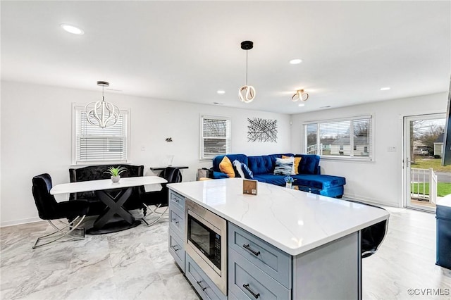 kitchen with gray cabinets, stainless steel microwave, open floor plan, a center island, and hanging light fixtures