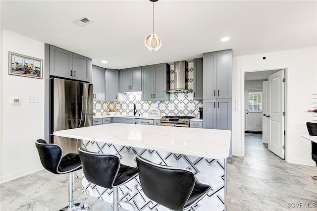 kitchen with gray cabinetry, light stone counters, appliances with stainless steel finishes, marble finish floor, and wall chimney exhaust hood