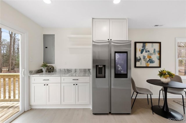 kitchen with stainless steel fridge, electric panel, white cabinets, and light wood-style flooring