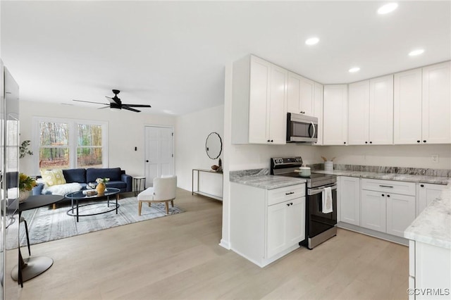 kitchen featuring light wood-style flooring, appliances with stainless steel finishes, open floor plan, light stone counters, and white cabinetry