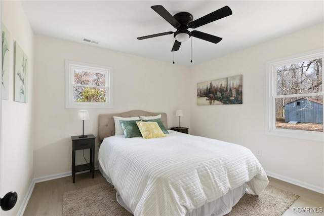 bedroom with baseboards, multiple windows, visible vents, and wood finished floors