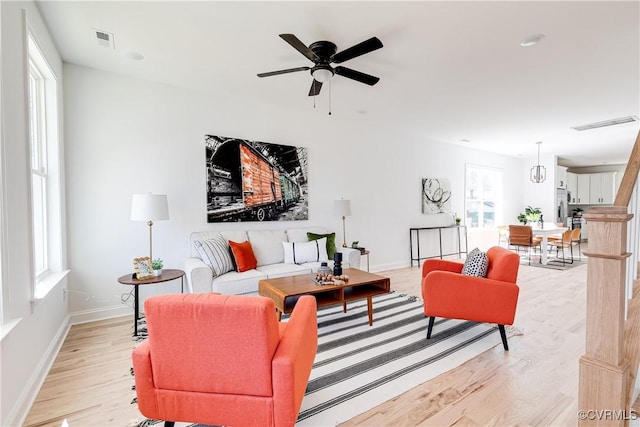 living room with light wood-type flooring, baseboards, visible vents, and a ceiling fan