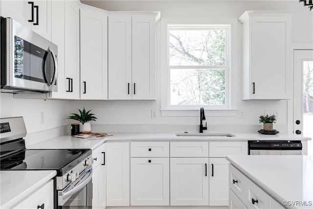 kitchen with stainless steel appliances, light countertops, a sink, and white cabinetry