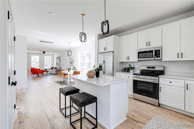 kitchen with light wood-style floors, open floor plan, a kitchen breakfast bar, appliances with stainless steel finishes, and a center island