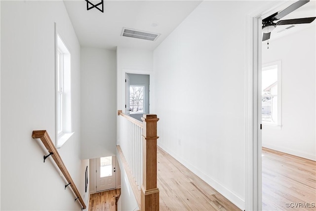 corridor with light wood-type flooring, baseboards, visible vents, and an upstairs landing