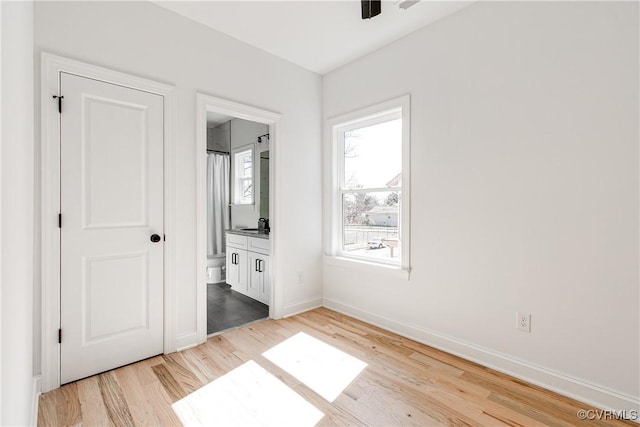 unfurnished bedroom with light wood-style floors, connected bathroom, and baseboards