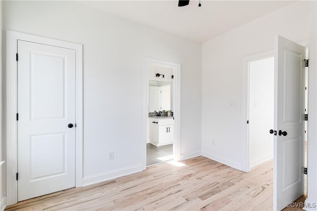 unfurnished bedroom featuring baseboards, ensuite bath, and light wood-style floors