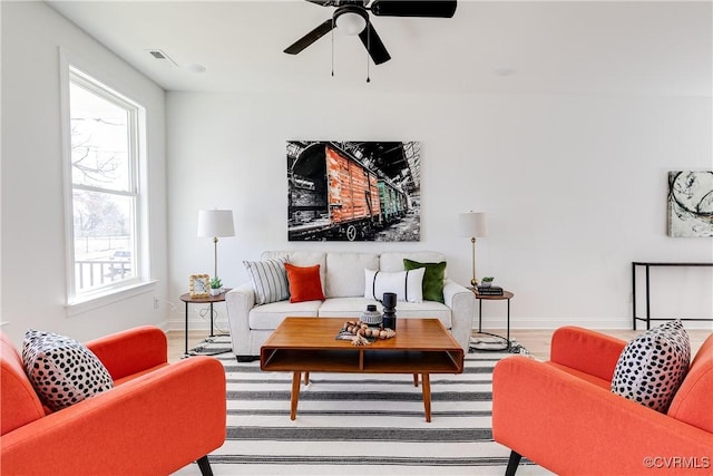 living room featuring visible vents, ceiling fan, baseboards, and wood finished floors