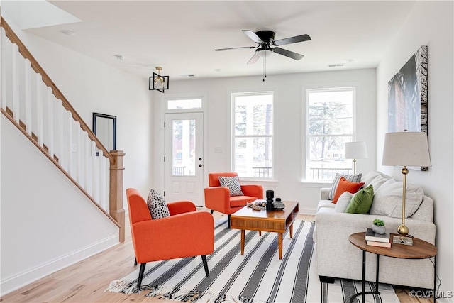 living room featuring ceiling fan, light wood-style flooring, baseboards, and stairs