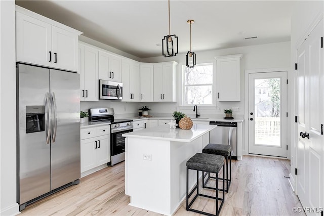 kitchen with light wood finished floors, a breakfast bar, stainless steel appliances, light countertops, and white cabinetry