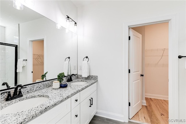 full bathroom with double vanity, wood finished floors, a sink, and a shower stall