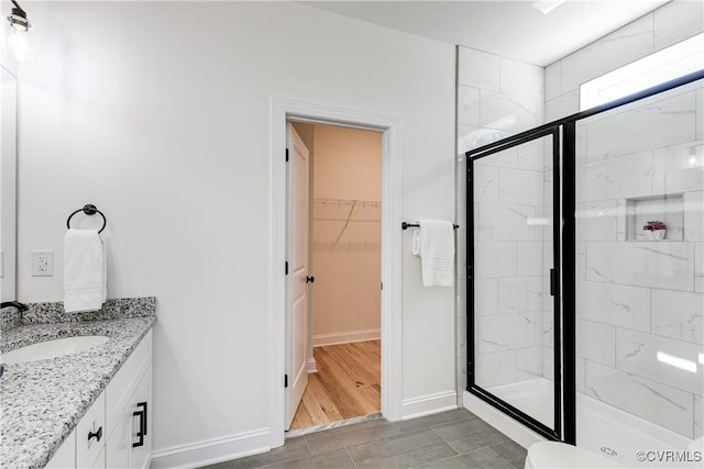 full bathroom with a stall shower, vanity, baseboards, and a spacious closet