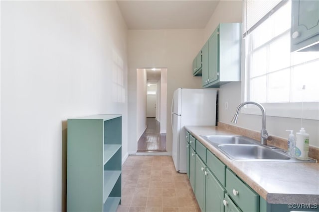 kitchen with open shelves, light countertops, freestanding refrigerator, a sink, and green cabinetry