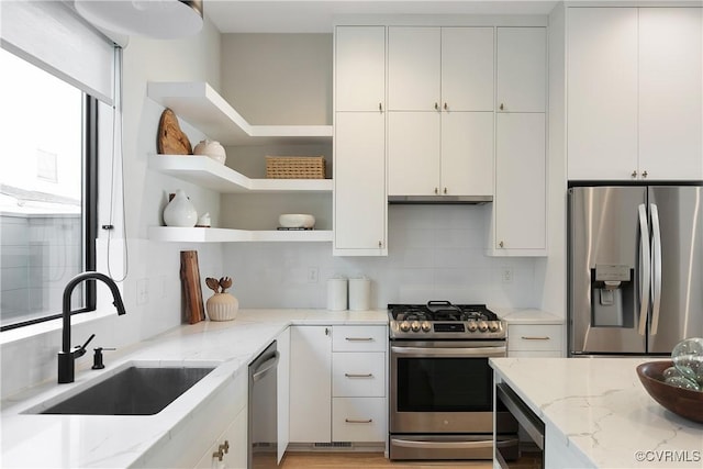 kitchen with light stone counters, open shelves, stainless steel appliances, white cabinetry, and a sink