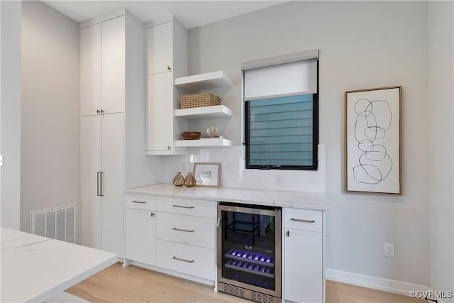 bar featuring beverage cooler, visible vents, light wood-style flooring, and baseboards