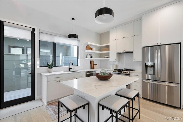 kitchen with a breakfast bar area, stainless steel appliances, a sink, open shelves, and pendant lighting