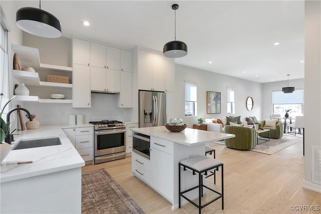 kitchen featuring white cabinets, appliances with stainless steel finishes, light wood-style floors, open shelves, and a sink