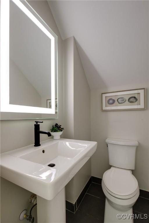 bathroom with toilet, vaulted ceiling, a sink, and tile patterned floors