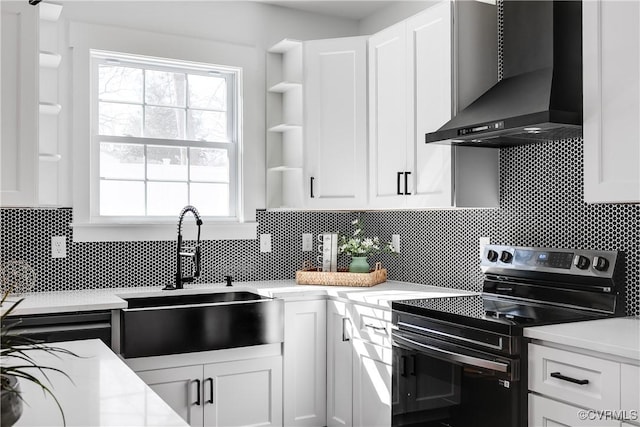 kitchen with a sink, white cabinetry, wall chimney range hood, open shelves, and stainless steel range with electric stovetop