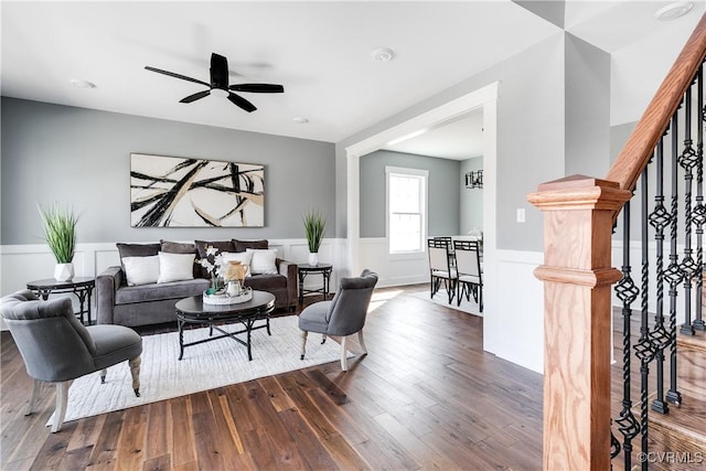 living area featuring a wainscoted wall, wood-type flooring, stairs, and a ceiling fan