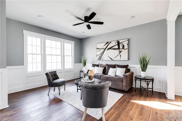 living area with a ceiling fan, a wainscoted wall, and wood finished floors