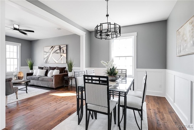 dining space featuring plenty of natural light, ceiling fan with notable chandelier, dark wood finished floors, and wainscoting