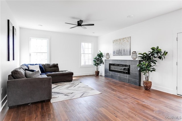 living room featuring ceiling fan, a fireplace, baseboards, and wood finished floors