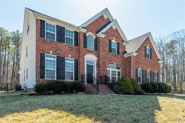 colonial-style house with central air condition unit, brick siding, and a front yard