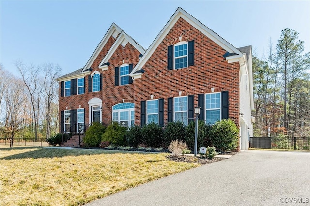 colonial inspired home featuring brick siding, fence, and a front lawn