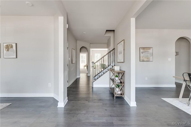 foyer with stairway, baseboards, dark wood-style floors, and arched walkways