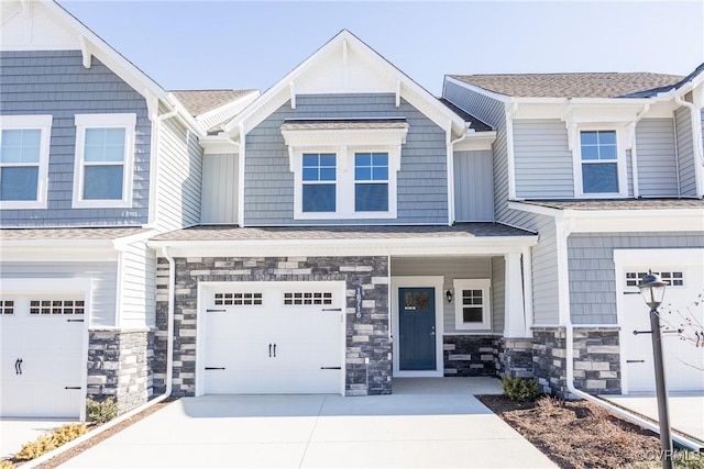 townhome / multi-family property featuring stone siding, roof with shingles, driveway, and an attached garage