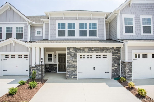 view of front of property with concrete driveway, stone siding, roof with shingles, an attached garage, and board and batten siding