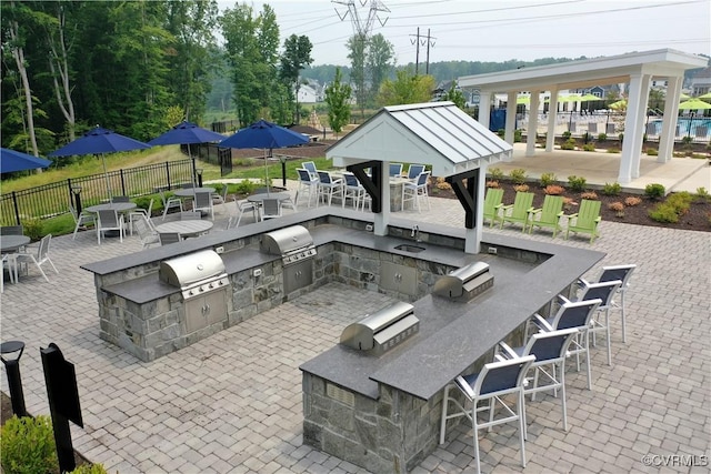 view of patio featuring outdoor wet bar, area for grilling, grilling area, fence, and a gazebo