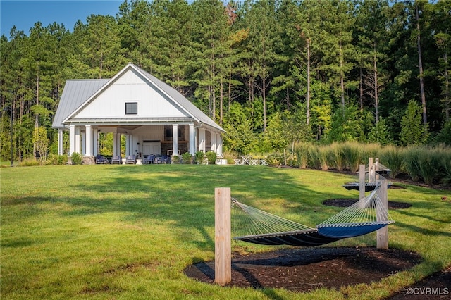 exterior space with metal roof, a lawn, and a view of trees