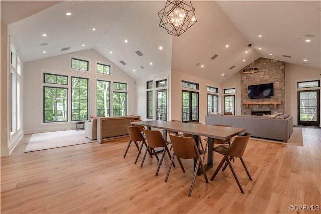 dining space featuring high vaulted ceiling, light wood-type flooring, visible vents, and a stone fireplace