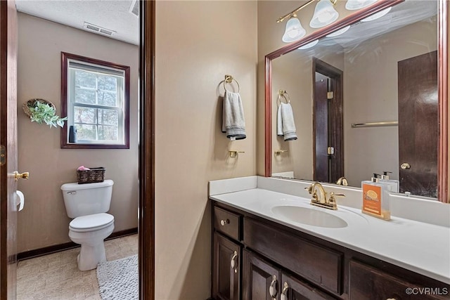 half bathroom with a textured ceiling, toilet, vanity, visible vents, and baseboards