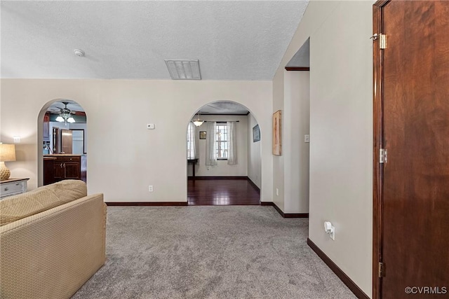 interior space with arched walkways, a textured ceiling, visible vents, baseboards, and carpet