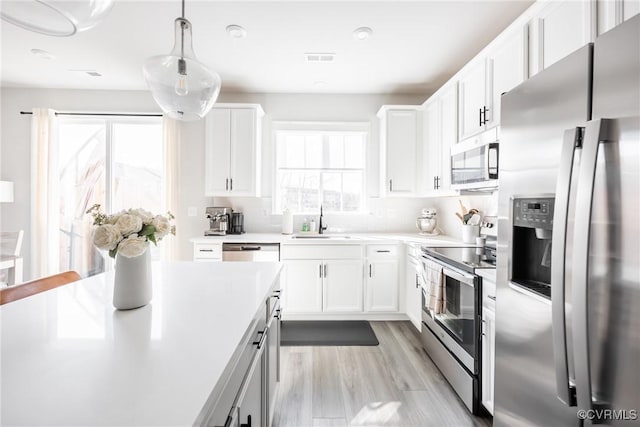 kitchen with appliances with stainless steel finishes, light countertops, a sink, and white cabinetry