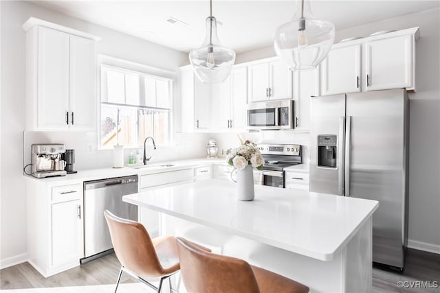 kitchen with stainless steel appliances, light countertops, white cabinetry, a sink, and a kitchen bar